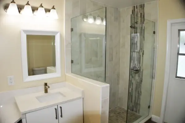 Remodeled bathroom with a white vanity, framed mirror and a corner frameless glass shower