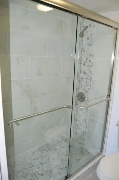 Tiled shower with mosaic accent column, pebble floor tile and a sliding glass enclosure