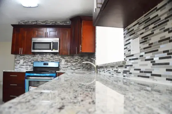 Dark wood cabinets with granite counters and a linear glass mosaic backsplash